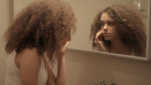 young girl with cosmeticorexia looking in the mirror